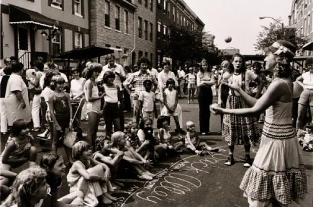A woman juggling in front of neighborhood children in Baltimore, MD (ca. 1975). Photograph by Joan Clark Netherwood.
