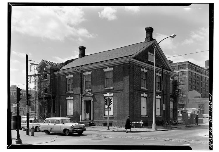 Black and white photo of two-story brick building with a car in front