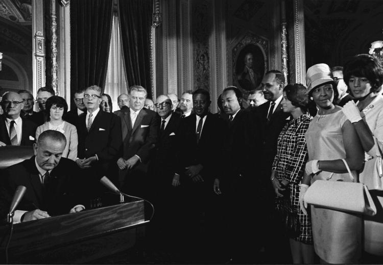 President Lyndon B. Johnson signs the Voting Rights Act of 1965 while Dr. Martin Luther King, Jr. and others look on.